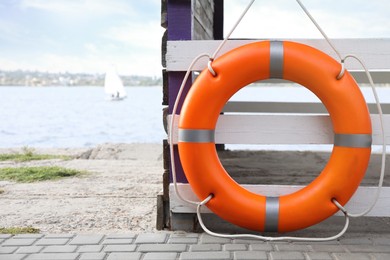 Orange life buoy hanging on white wooden fence at beach, space for text
