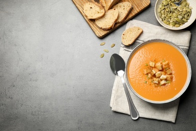 Tasty creamy pumpkin soup served with bread and seeds on grey table, flat lay. Space for text