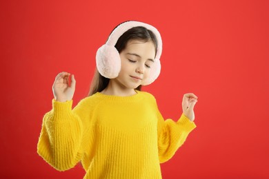 Cute girl wearing stylish earmuffs on red background