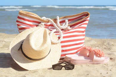 Stylish striped bag with summer accessories on sandy beach near sea