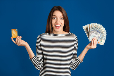 Excited young woman with cash money and credit card on blue background