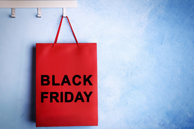 Paper shopping bag with phrase BLACK FRIDAY on rack near blue wall, space for text