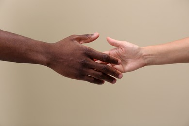 Woman and African American man shaking hands on beige background, closeup