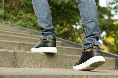 Man in stylish black sneakers walking up stairs, closeup