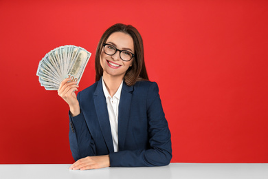 Young woman with money at table on crimson background