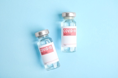 Vials with coronavirus vaccine on light blue background, flat lay