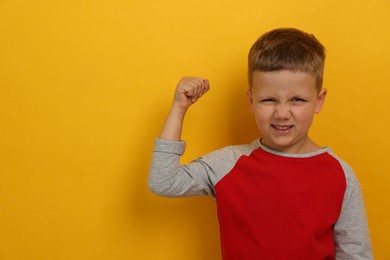 Angry little boy on yellow background, space for text. Aggressive behavior