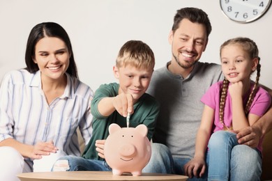 Happy family putting money into piggy bank at table in room