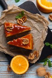 Photo of Pieces of delicious caramel cheesecake with walnuts and orange served on wooden table, flat lay