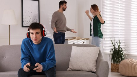 Teenage boy playing videogame while his parents arguing on background. Problems at home