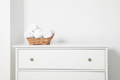 Soft rolled towels in wicker basket on white chest of drawers