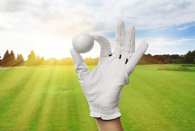 Player holding golf ball in park on sunny day, closeup