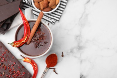 Photo of Cup of hot chocolate with chili pepper and cinnamon on white marble table, flat lay. Space for text