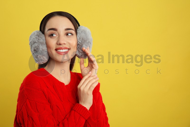 Beautiful young woman wearing earmuffs on yellow background. Space for text