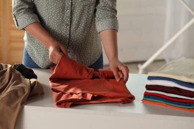 Woman folding clothes at white table indoors, closeup
