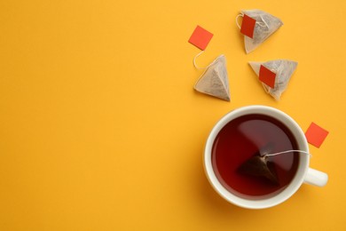 Tea bags and cup of hot drink on orange background, flat lay. Space for text