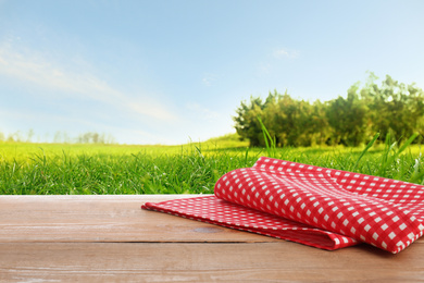 Picnic wooden table with checkered red napkin and picturesque landscape on background