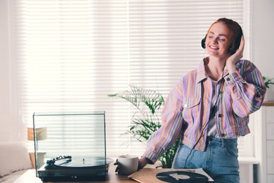 Young woman drinking coffee while listening to music with turntable at home