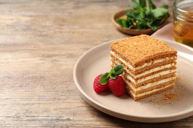 Slice of delicious layered honey cake served with mint and raspberries on wooden table. Space for text
