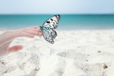 Woman holding beautiful rice paper butterfly on sandy beach, closeup