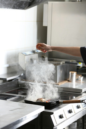 Female chef cooking meal on stove in restaurant kitchen, closeup