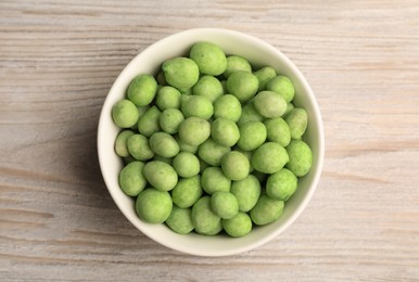Tasty wasabi coated peanuts in bowl on white wooden table, top view