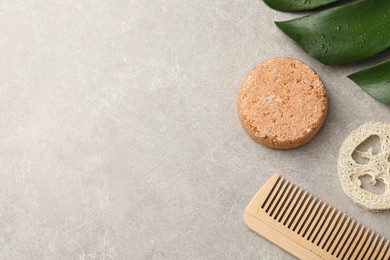 Solid shampoo bar, monstera leaf, comb and loofah on grey table, flat lay. Space for text