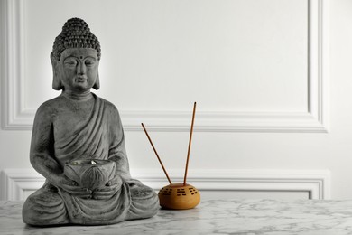 Buddha statue and incense sticks on white marble table. Space for text
