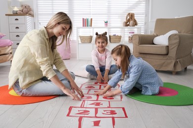 Mother and little girls taping sticker hopscotch on floor at home