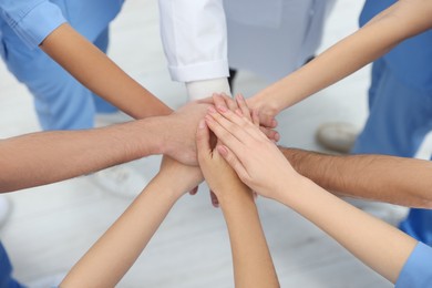 Photo of Doctor and interns stacking hands together indoors, closeup