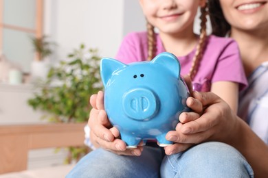 Photo of Closeup view of woman and her daughter with piggy bank at home