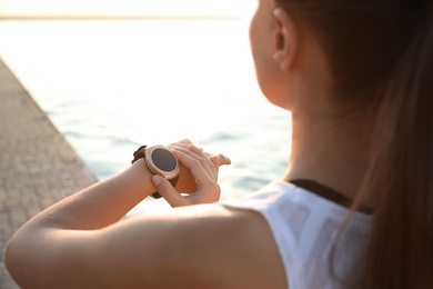 Woman checking fitness tracker after training near river, closeup