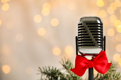 Microphone with red bow and fir branches against blurred lights, space for text. Christmas music