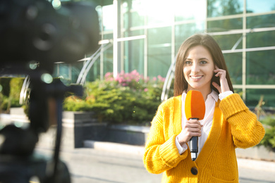 Young female journalist with microphone working on city street