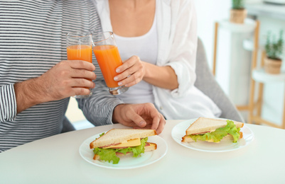 Photo of Young couple having breakfast with sandwiches at table in kitchen, closeup