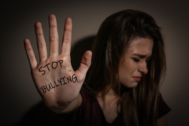 Abused teen girl showing palm with message STOP BULLYING near beige wall, focus on hand