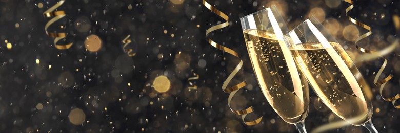 Glasses with sparkling wine and shiny serpentine streamers against blurred festive lights, space for text. Banner design
