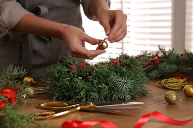 Florist making beautiful Christmas wreath at wooden table indoors, closeup