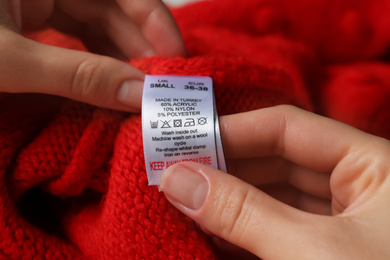 Woman reading clothing label with care symbols and material content on red knitted sweater, closeup