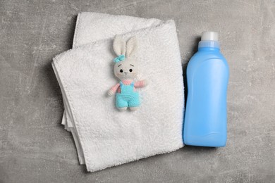 Bottle of laundry detergent, clean towel and rabbit toy on light grey table, flat lay