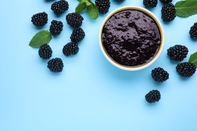 Blackberry puree in bowl and fresh berries on light blue background, flat lay. Space for text