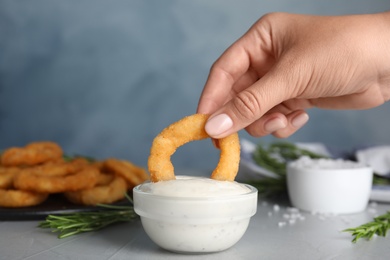 Woman dipping crunchy fried onion ring in sauce, closeup
