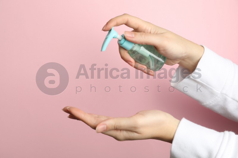 Woman applying antiseptic gel on hand against pink background, closeup