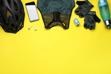Flat lay composition with different cycling accessories and clothes on yellow background, space for text