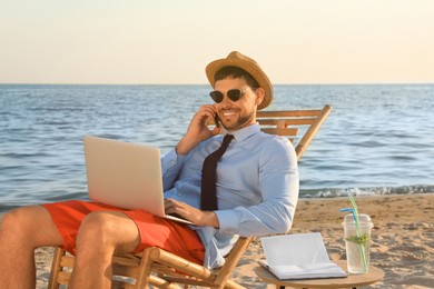 Photo of Man with laptop talking by mobile phone on beach. Business trip