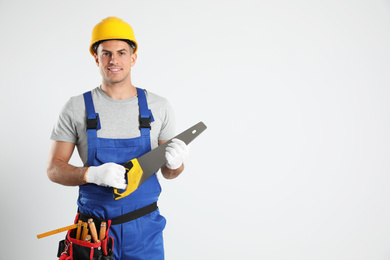 Carpenter with tool belt and hand saw on light background. Space for text