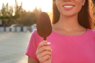 Young woman holding ice cream glazed in chocolate on city street, closeup