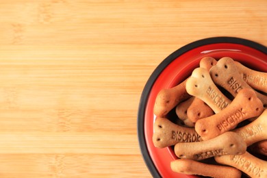 Photo of Bone shaped dog cookies in feeding bowl on wooden table, top view. Space for text