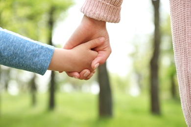 Little child holding hands with his mother outdoors, closeup. Family time