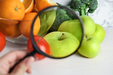 Woman with magnifying glass exploring vegetables and fruits, closeup. Poison detection